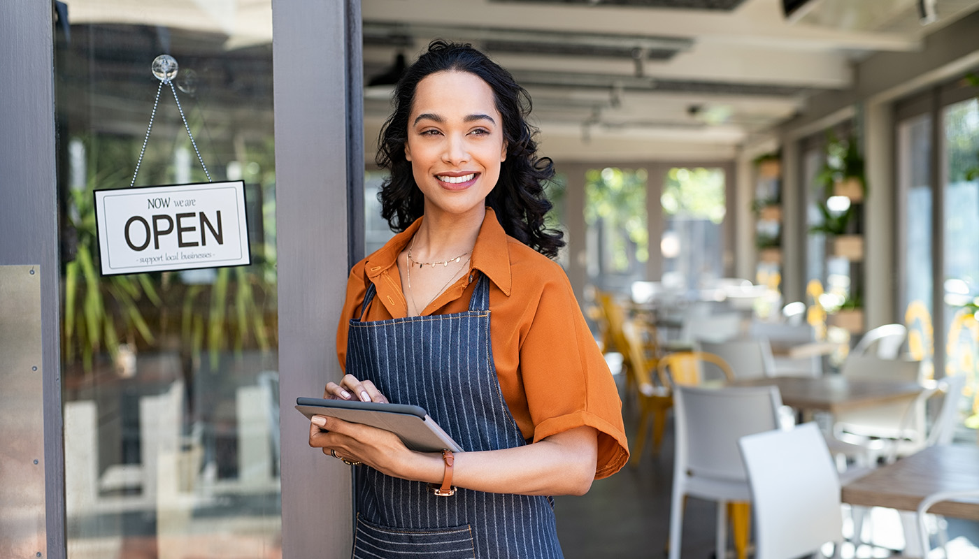 Welcoming woman outside café with 'OPEN' sign, representing C&D Advisory's tax services for small businesses.